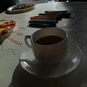 Eine gefüllte Kaffeetasse steht auf einem beschrifteten Flipchart. Die Sonne scheint auf den Tisch.